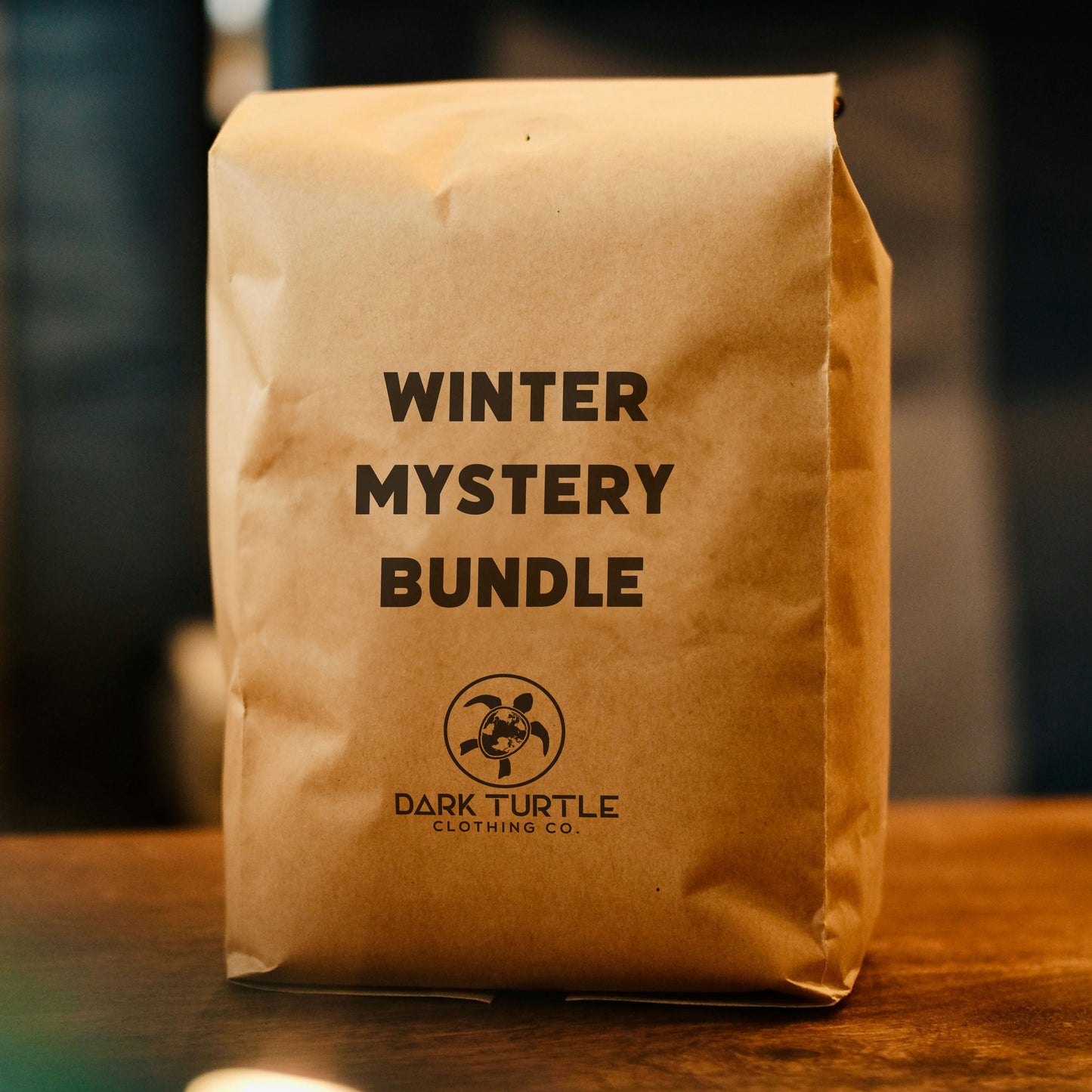 Brown paper bag with 'Winter Mystery Bundle' text and Dark Turtle Clothing Co logo on a wooden surface.