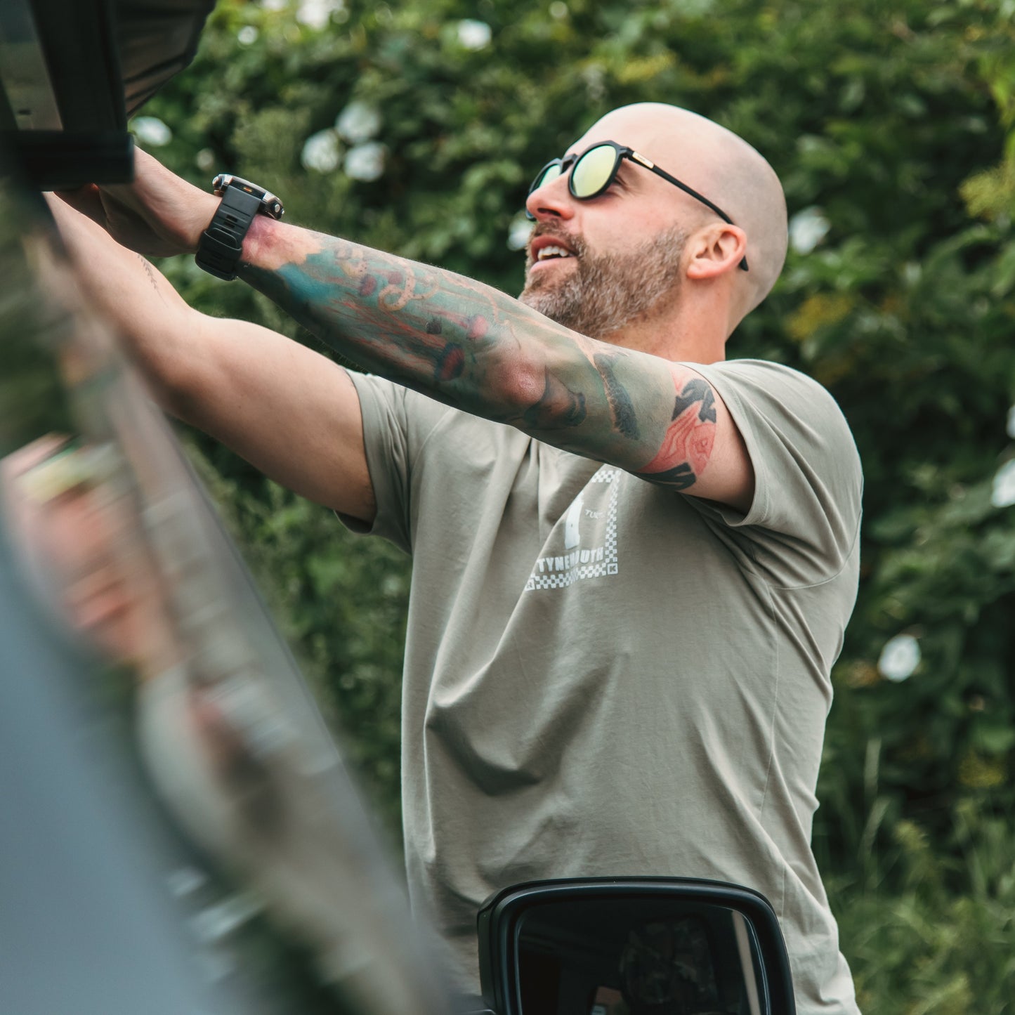 Man with tattoos and sunglasses adjusting something on a vehicle outdoors