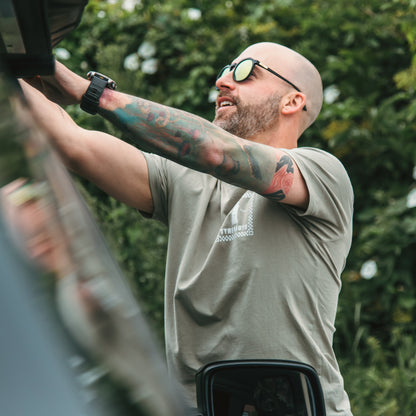 Man with tattoos and sunglasses adjusting something on a vehicle outdoors