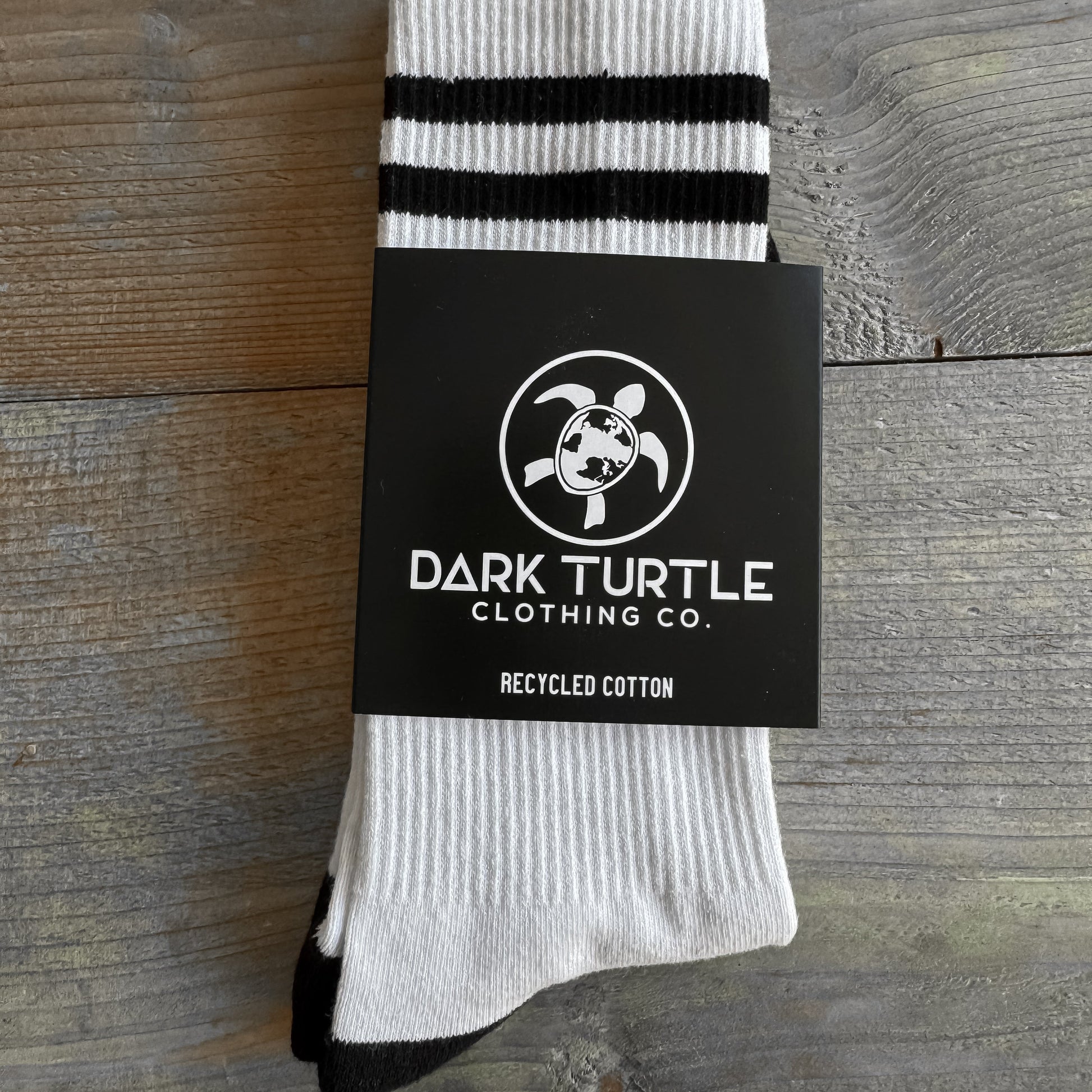 White sock with black stripes on a wooden surface, featuring Dark Turtle Clothing Co. branding.