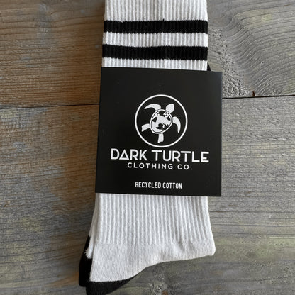 White sock with black stripes on a wooden surface, featuring Dark Turtle Clothing Co. branding.